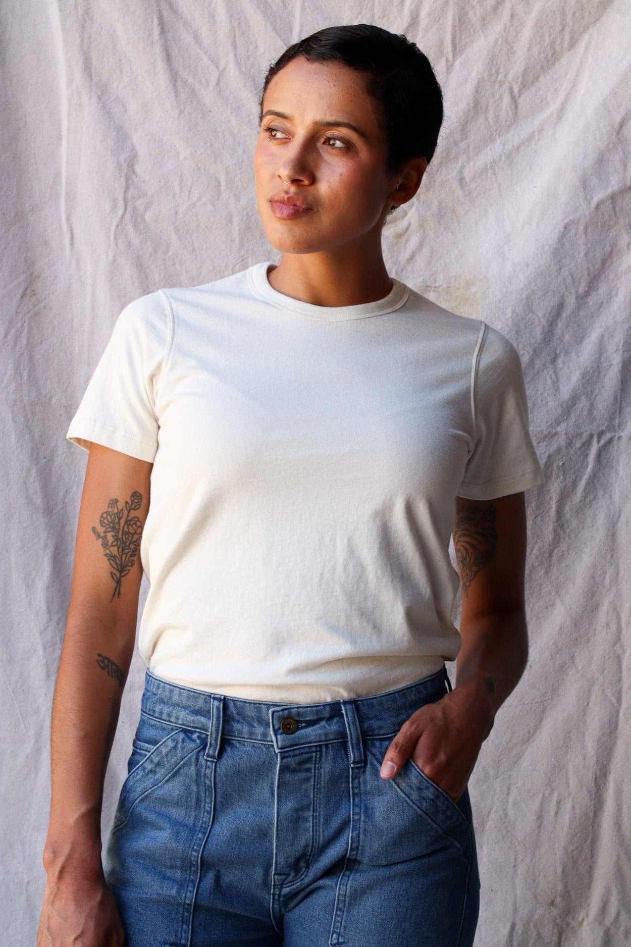 Woman wearing a natural cream Bolinas heavyweight cotton tee tucked into blue jeans against a linen backdrop.