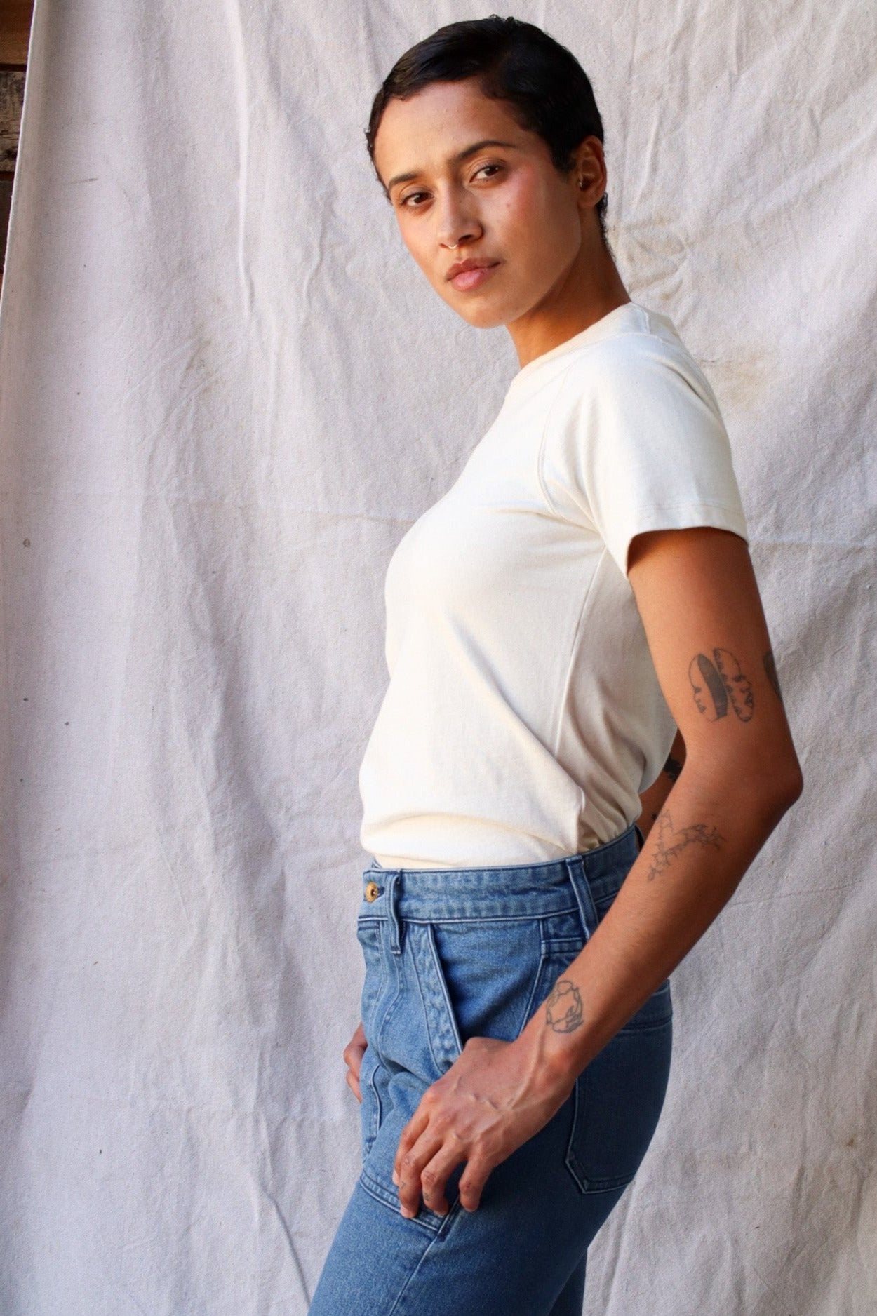 Side view of a model wearing the natural heavyweight cotton Bolinas tee with blue jeans against a canvas backdrop.