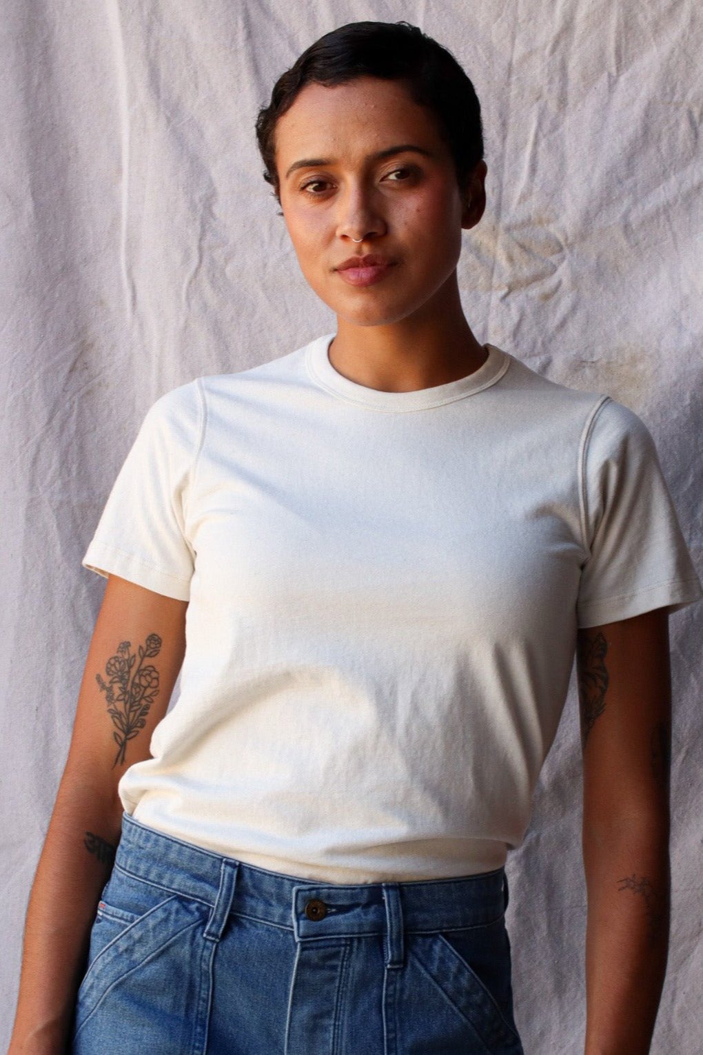 Woman wearing a natural cream heavyweight cotton tee tucked into blue denim jeans.