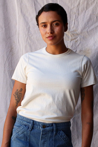 Woman wearing a natural cream heavyweight cotton tee tucked into blue denim jeans.