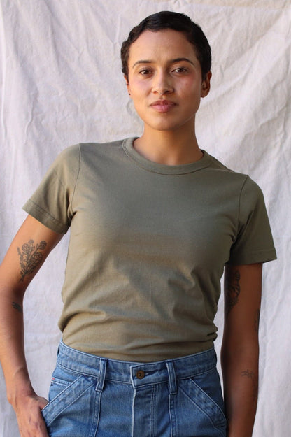 Model wearing an olive heavyweight cotton crewneck tee with blue denim jeans against a linen backdrop.