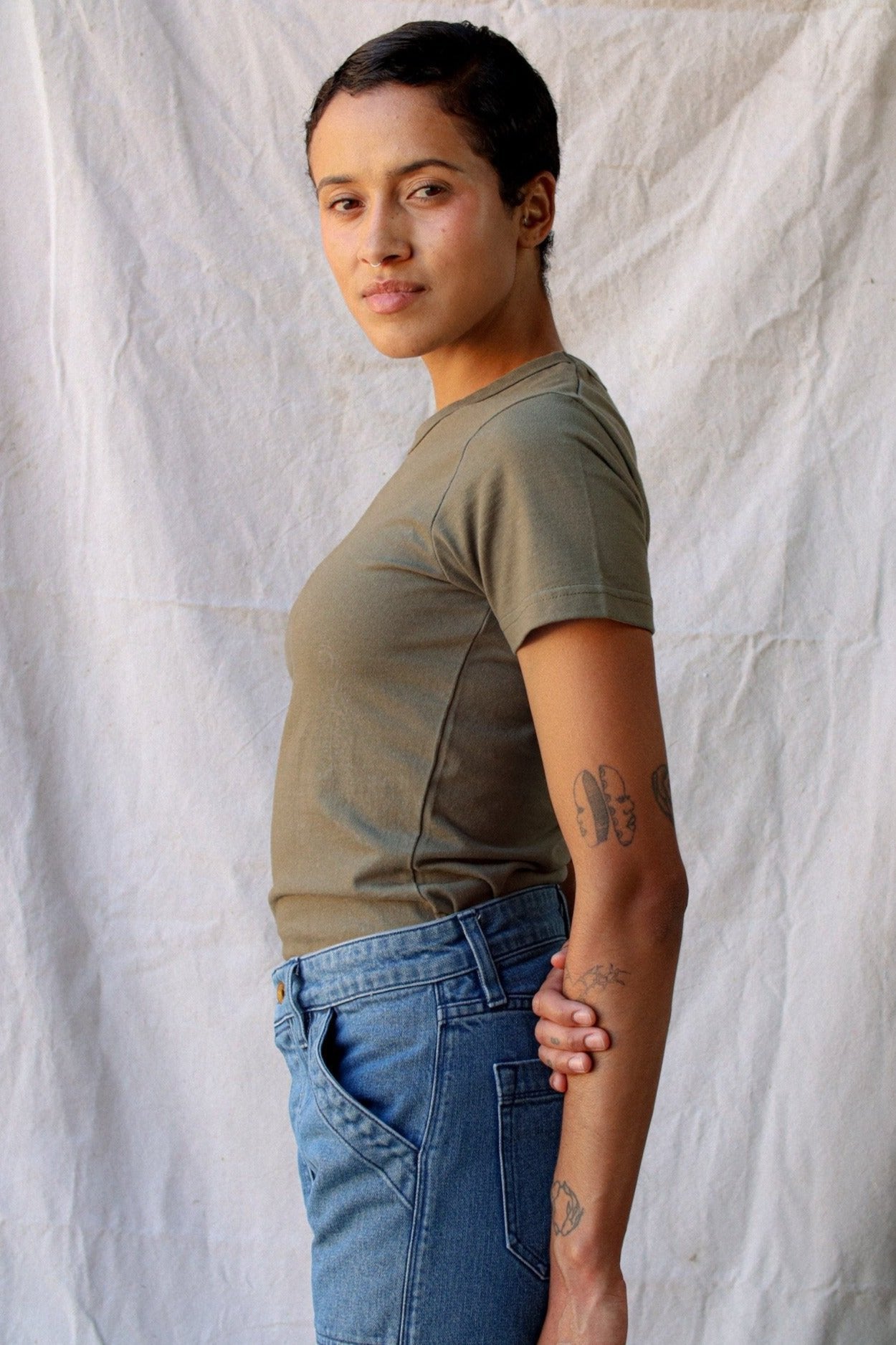 Side profile of a model wearing the olive Bolinas heavyweight tee with blue jeans against a canvas backdrop.