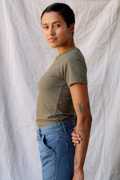 Side profile of a model wearing the olive Bolinas heavyweight tee with blue jeans against a canvas backdrop.