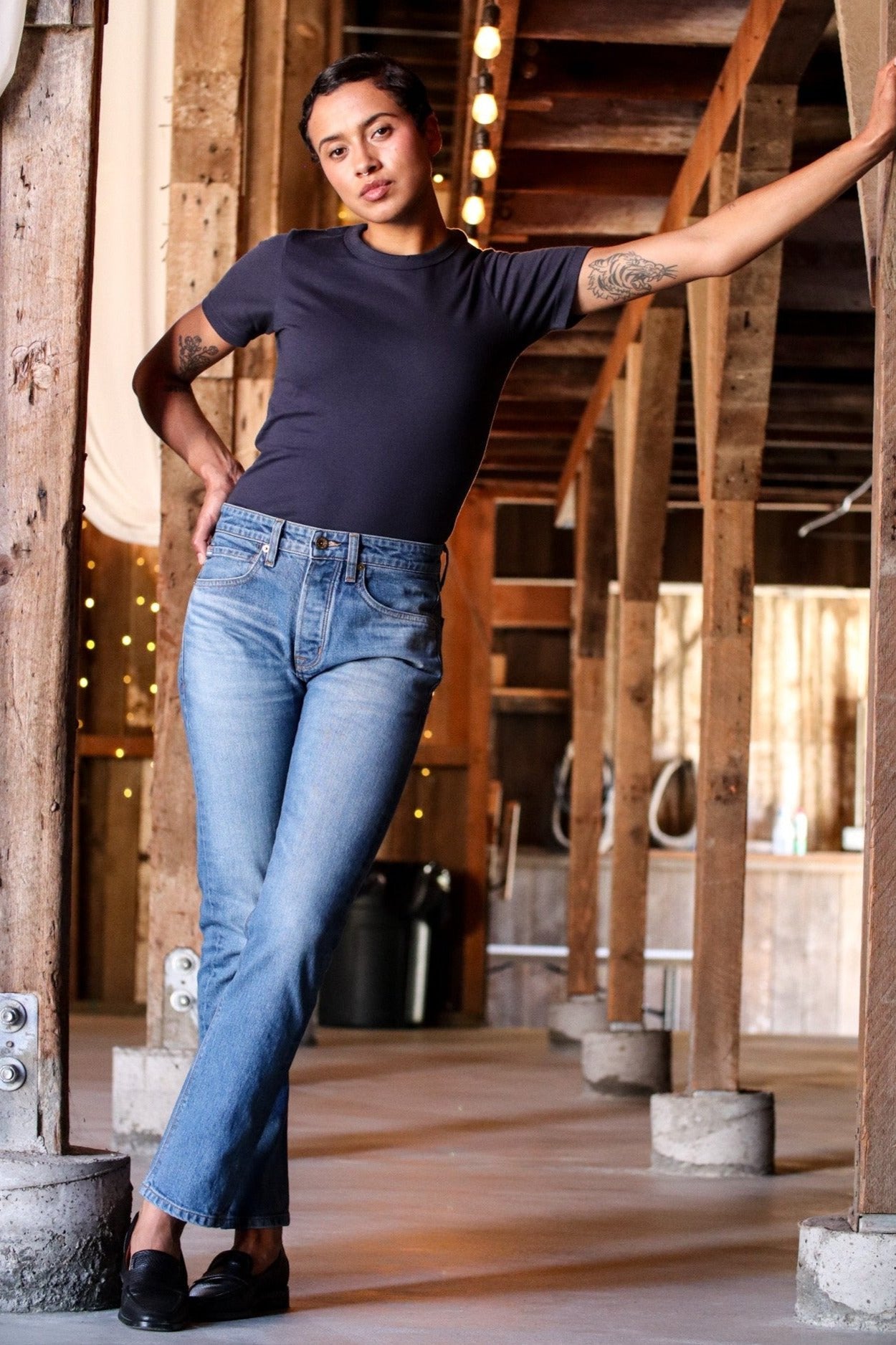 Model wearing the navy Bolinas heavyweight tee with blue jeans in a rustic timber-framed space.
