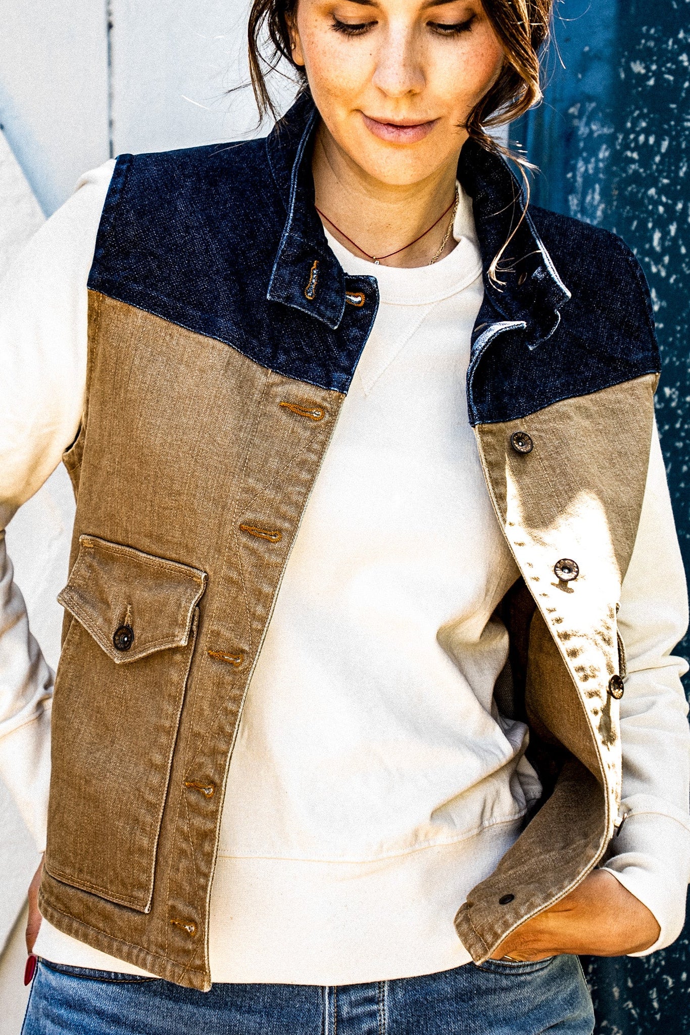 Woman wearing wheat broken twill denim vest with contrast navy yoke and brass buttons.