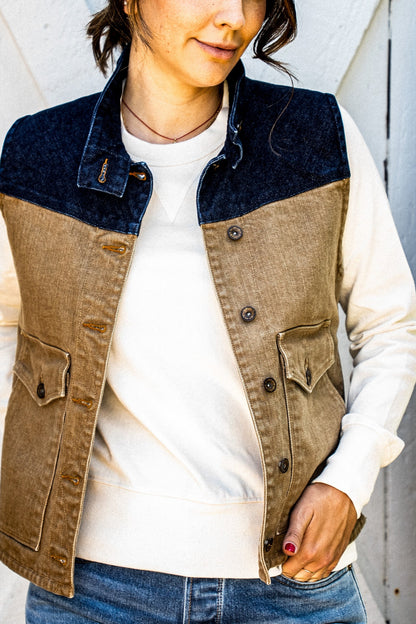 Wheat broken twill denim Jamie vest with navy yoke, worn open over a cream sweatshirt.