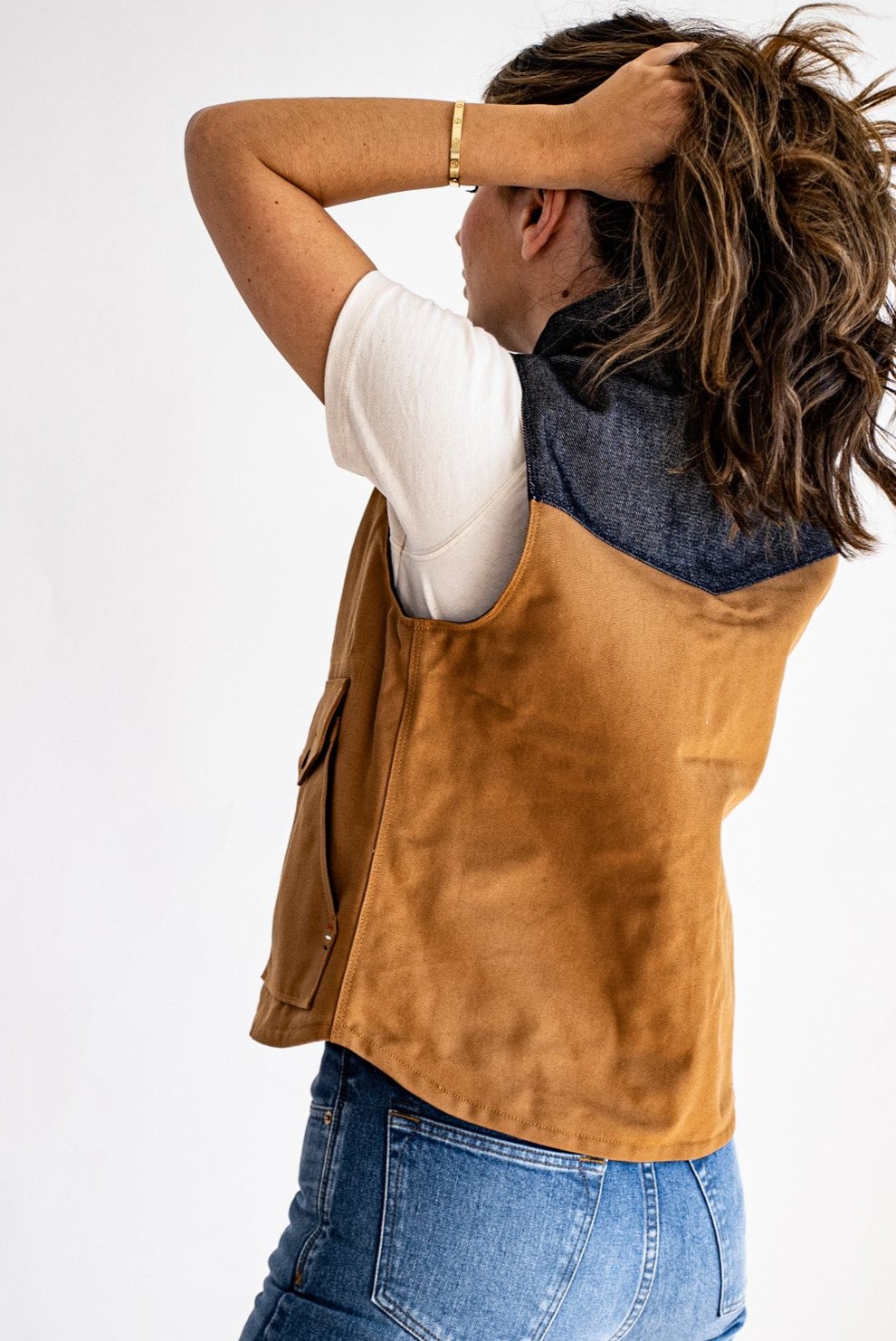 Back view of the Jamie Vest in tan canvas with a denim yoke, worn over a white tee with blue jeans.