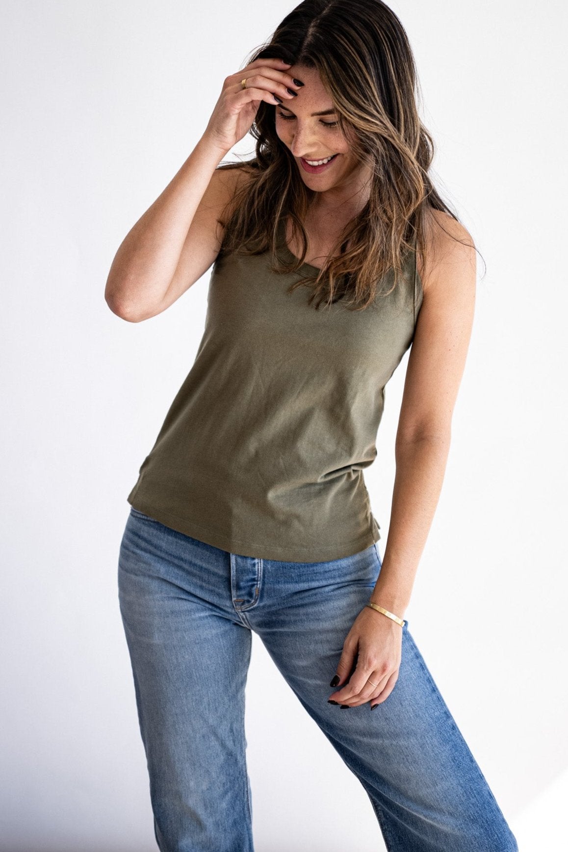 Woman wearing an olive Reyes cotton tank top styled with light-wash denim jeans.