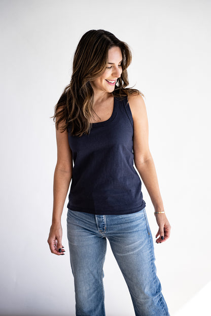 Woman wearing a dark navy scoop-neck cotton tank top with light wash jeans against a white backdrop.