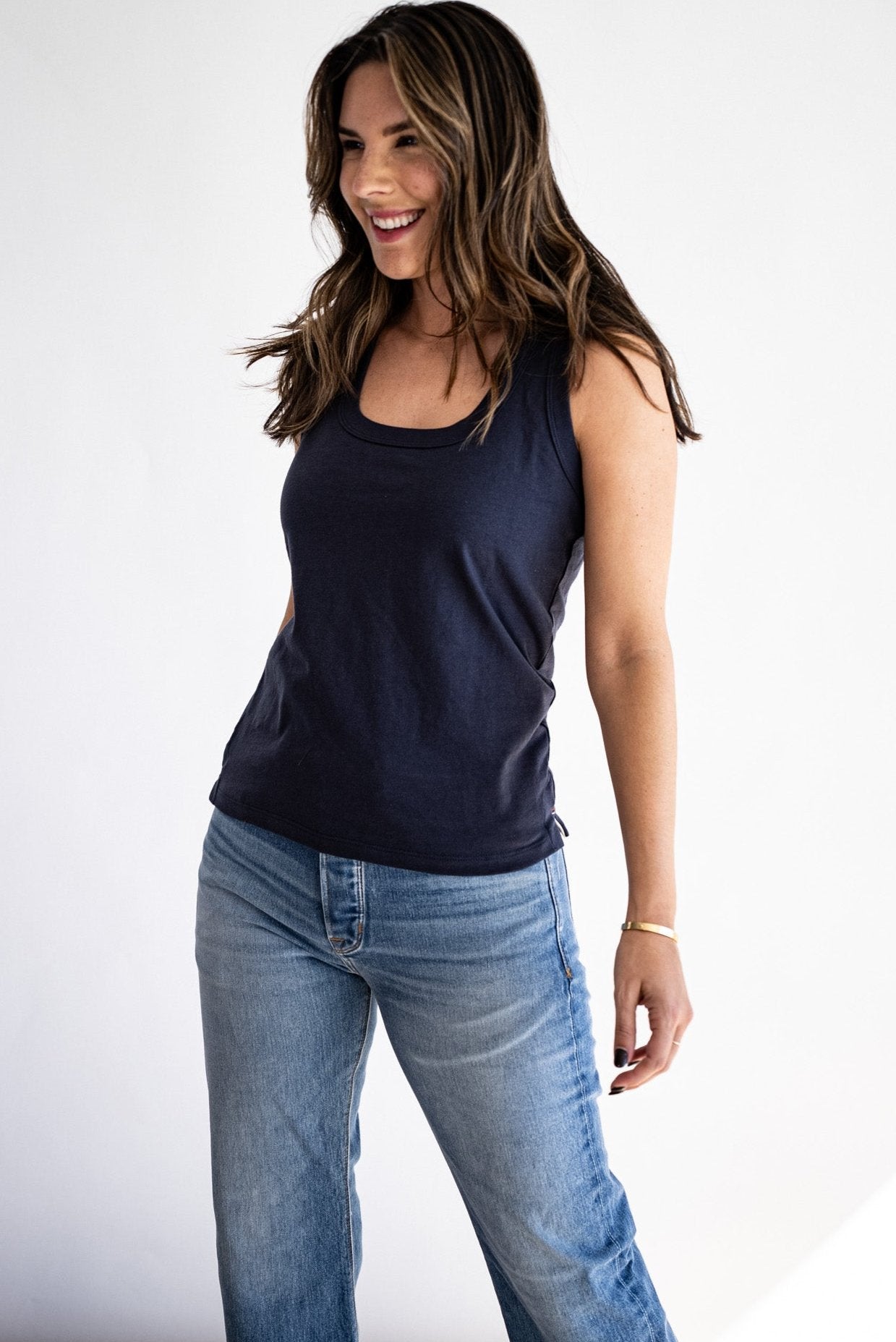 Woman wearing a navy cotton scoop-neck tank top with light wash denim jeans.