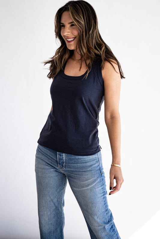 Woman wearing a navy cotton scoop-neck tank top with light wash denim jeans.