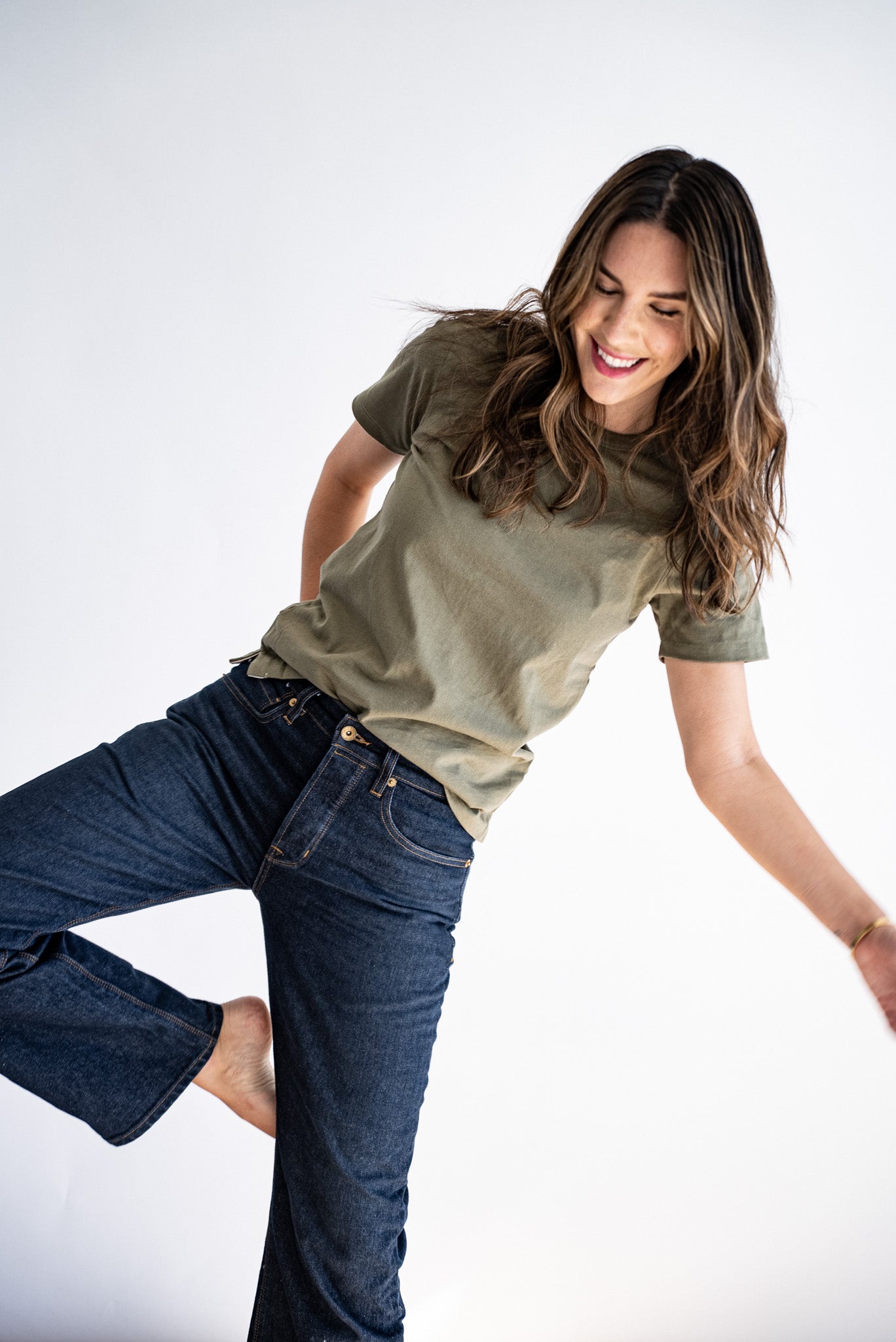 Model wearing the olive Reyes boxy tee with dark raw denim jeans, laughing mid-step.