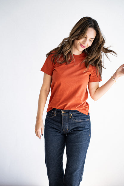 Reyes boxy tee in brick red cotton, styled with dark denim jeans against a white backdrop.