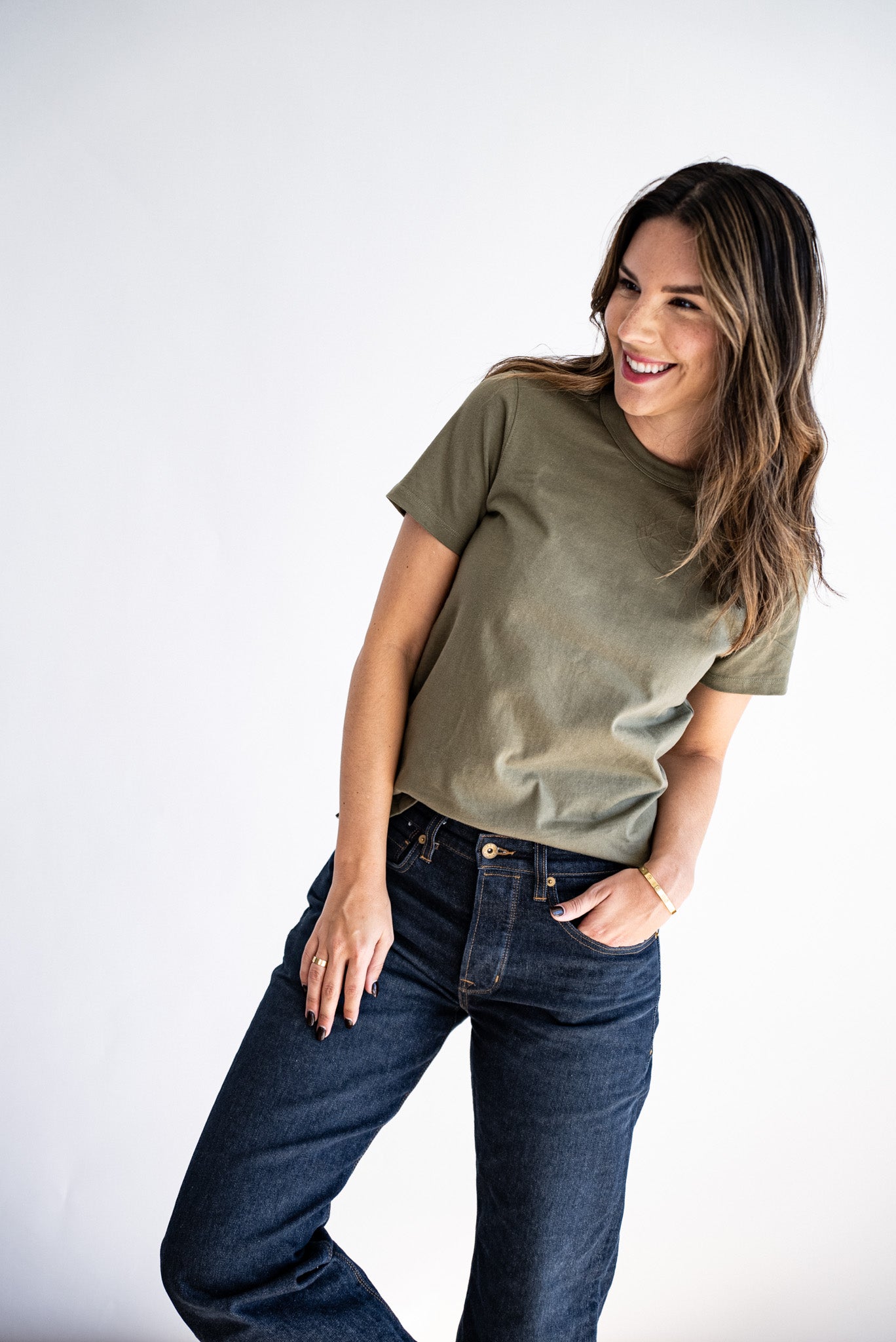 Woman wearing an olive Reyes boxy tee tucked into dark raw denim jeans.