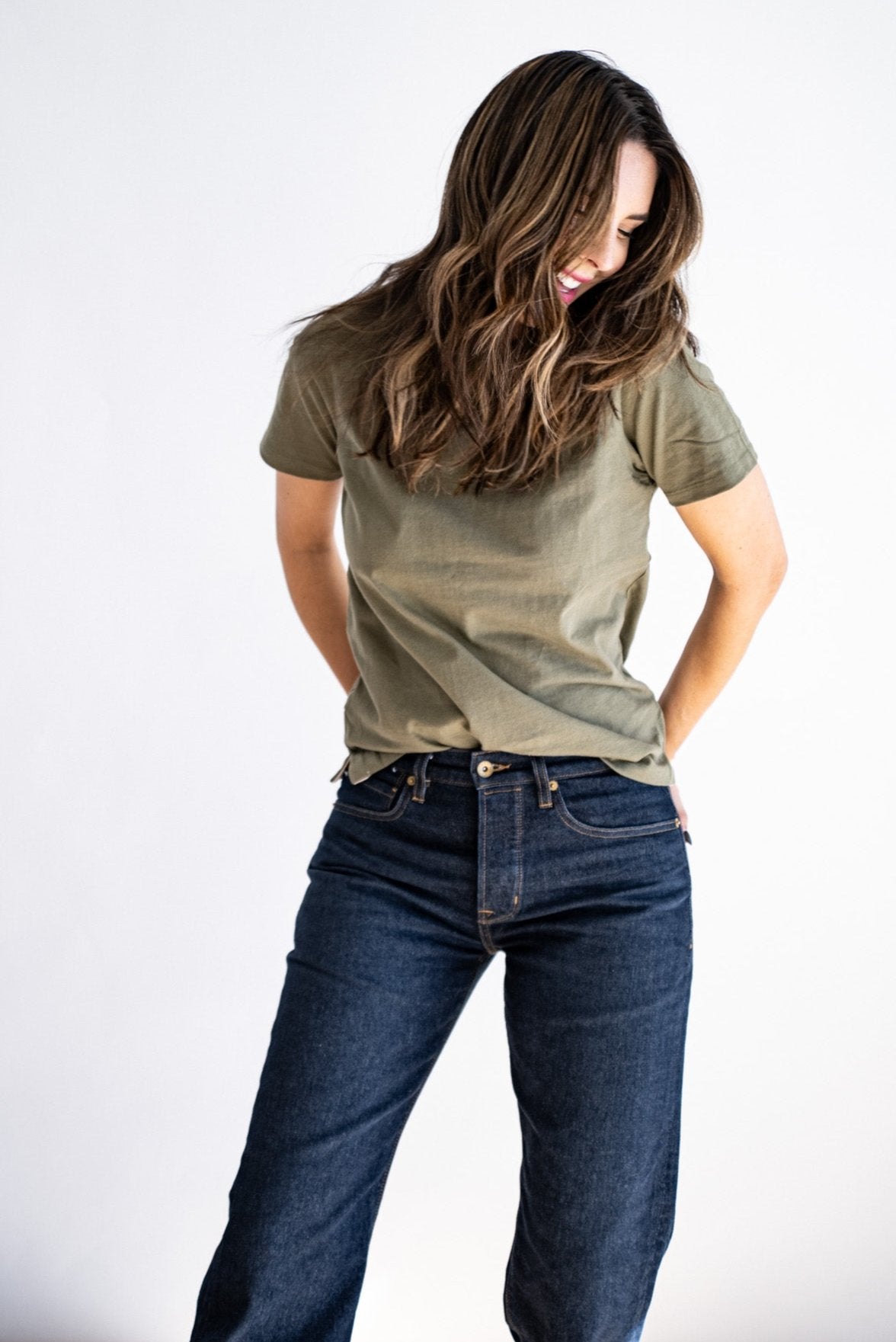 Olive green boxy tee styled with dark wash denim jeans, hands tucked in back pockets.