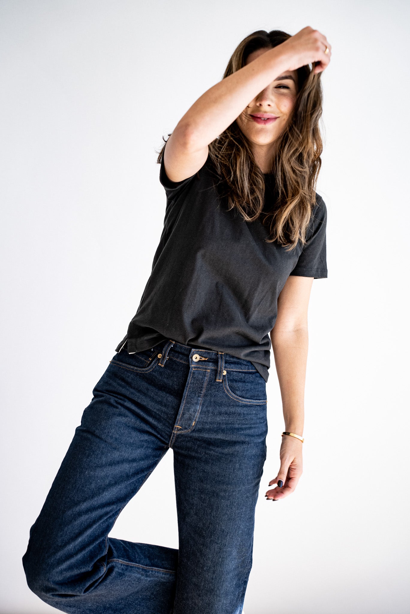 Woman wearing the Reyes boxy tee in basalt black, styled untucked with dark raw denim jeans.
