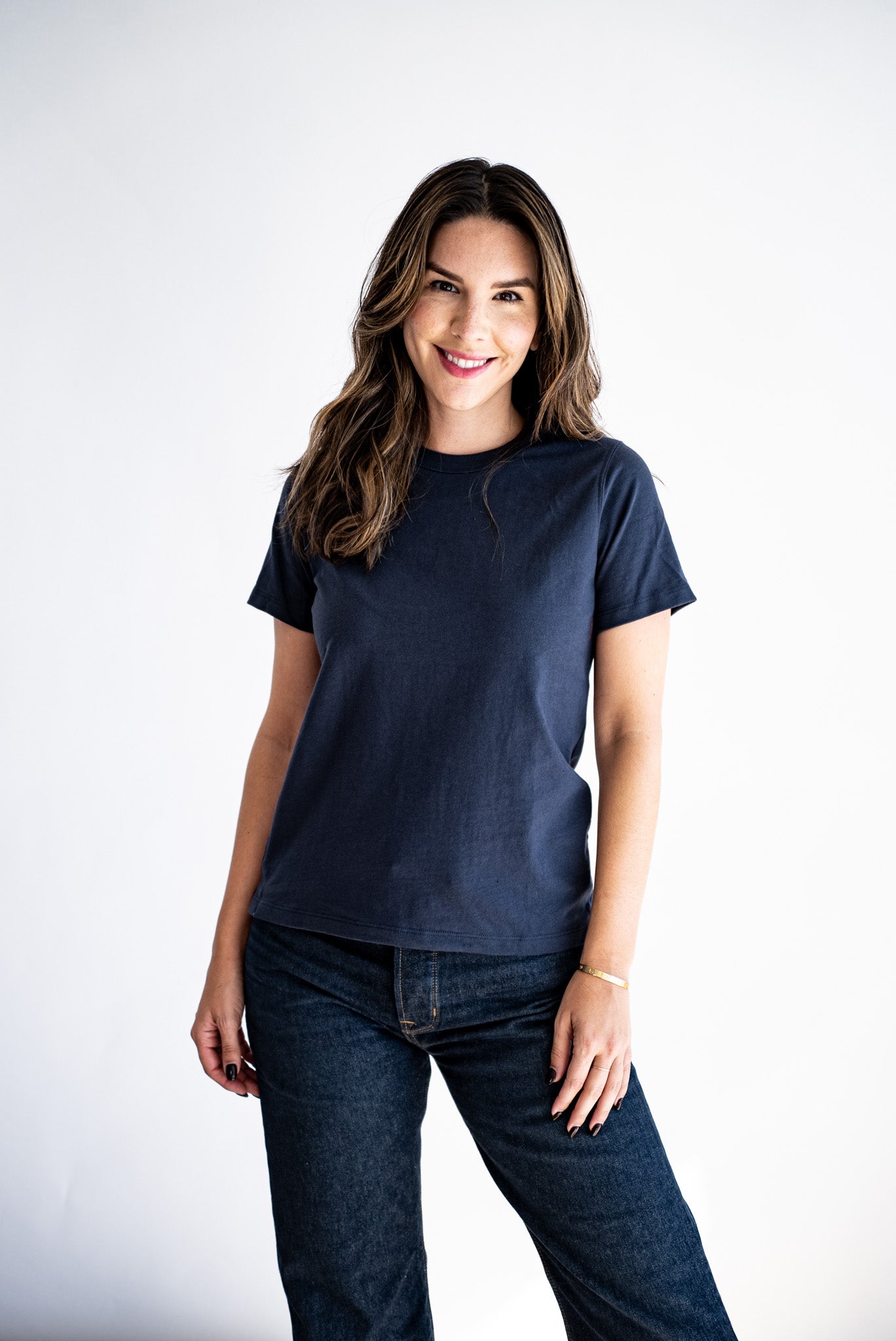 Woman wearing a navy boxy crewneck tee with dark denim jeans against a white studio backdrop.