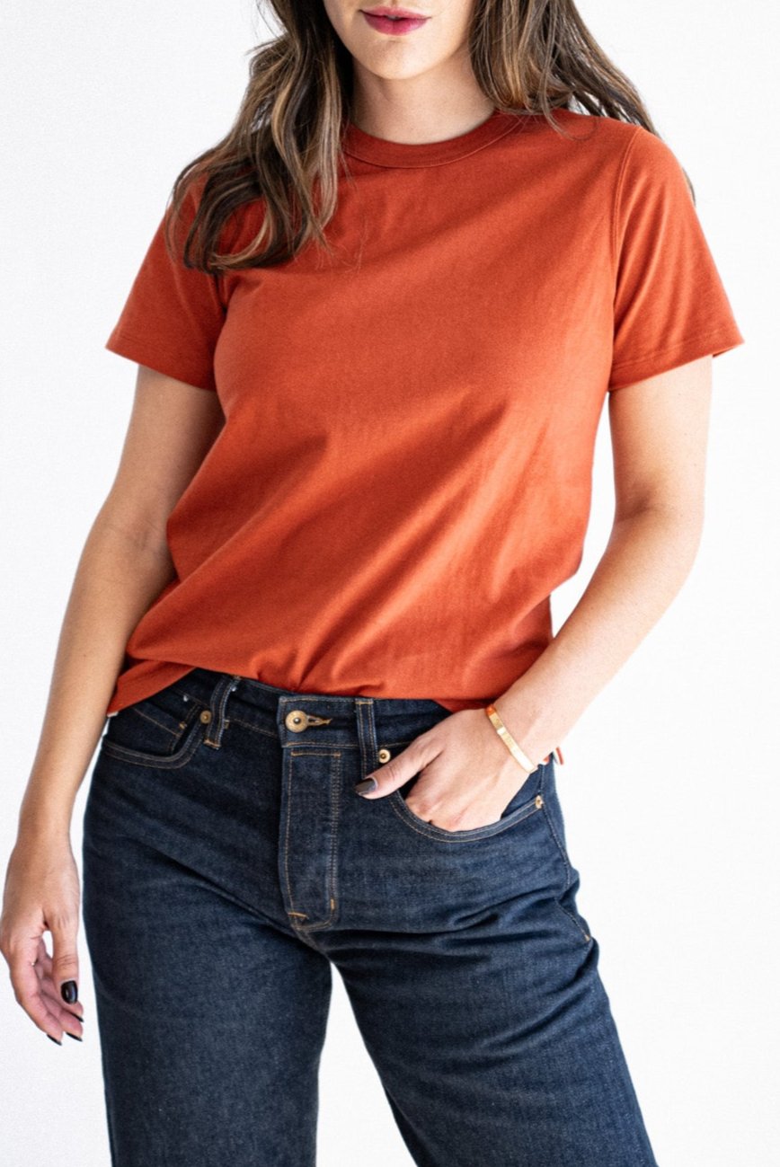 Brick-colored boxy cotton tee styled with dark raw denim jeans and a gold bracelet.