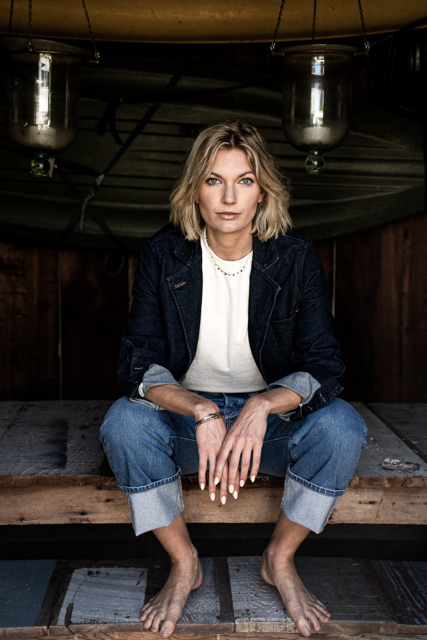 Model in dark ocean denim Scout Blazer with rolled cuffs, white tee, and cuffed jeans on a wooden platform.