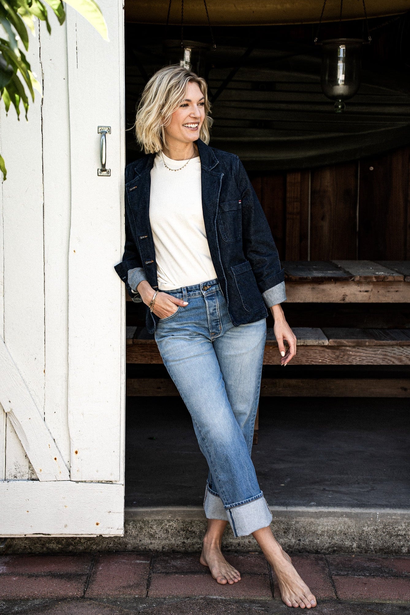Model in ocean-blue denim chore blazer over a cream tee and light-wash cuffed jeans, leaning in a doorway.