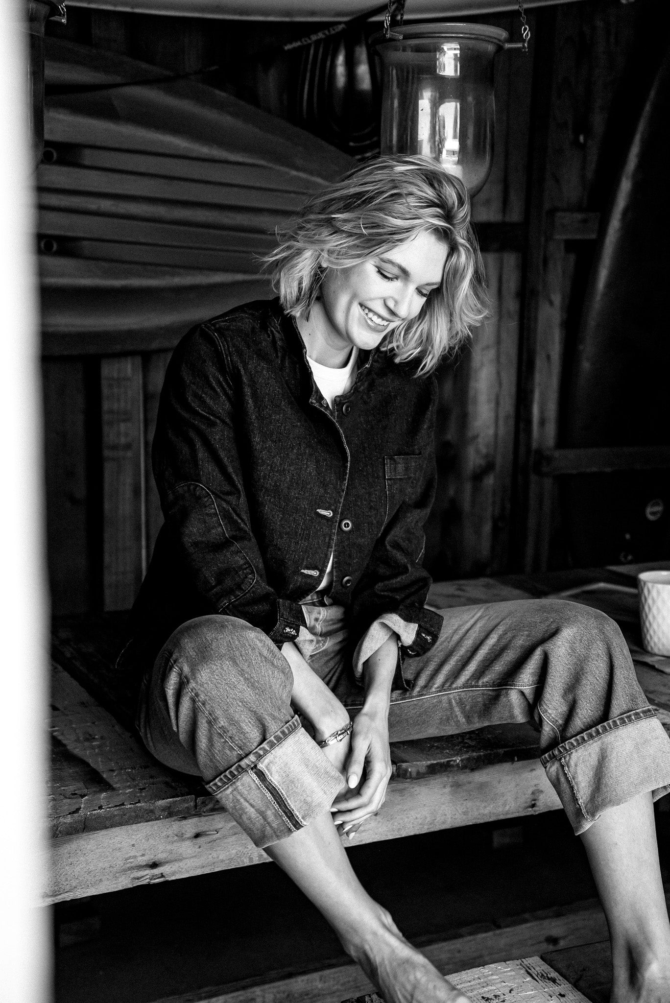Model in the Scout denim chore blazer and cuffed jeans, seated on a wooden boat dock.