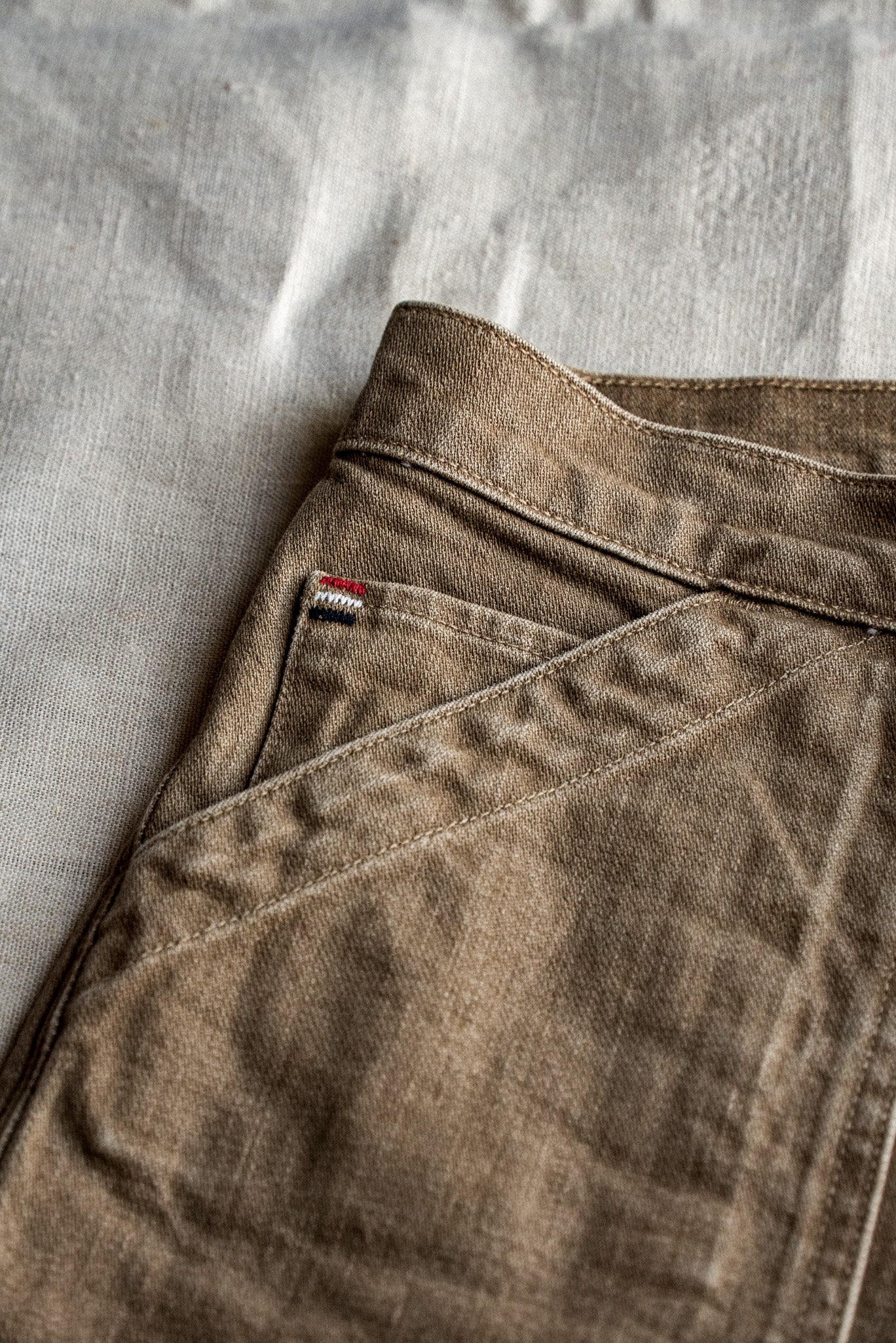 Close-up of wheat-colored denim shorts showing waistband, pocket stitching, and woven selvedge tab.