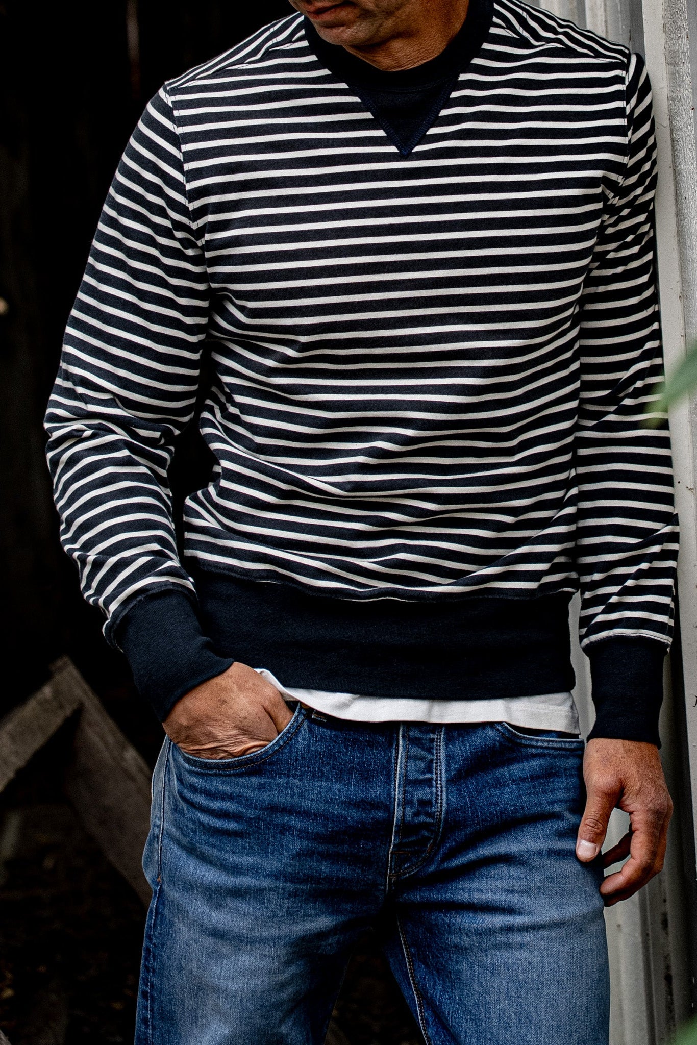 Man wearing the navy and white striped Stinson rugby jersey pullover with blue denim jeans.