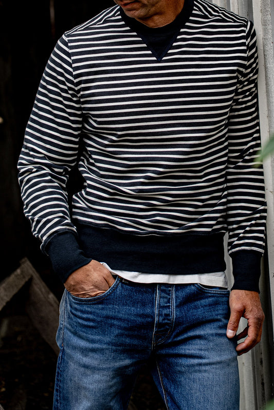 Man wearing the navy and white striped Stinson rugby jersey pullover with blue denim jeans.