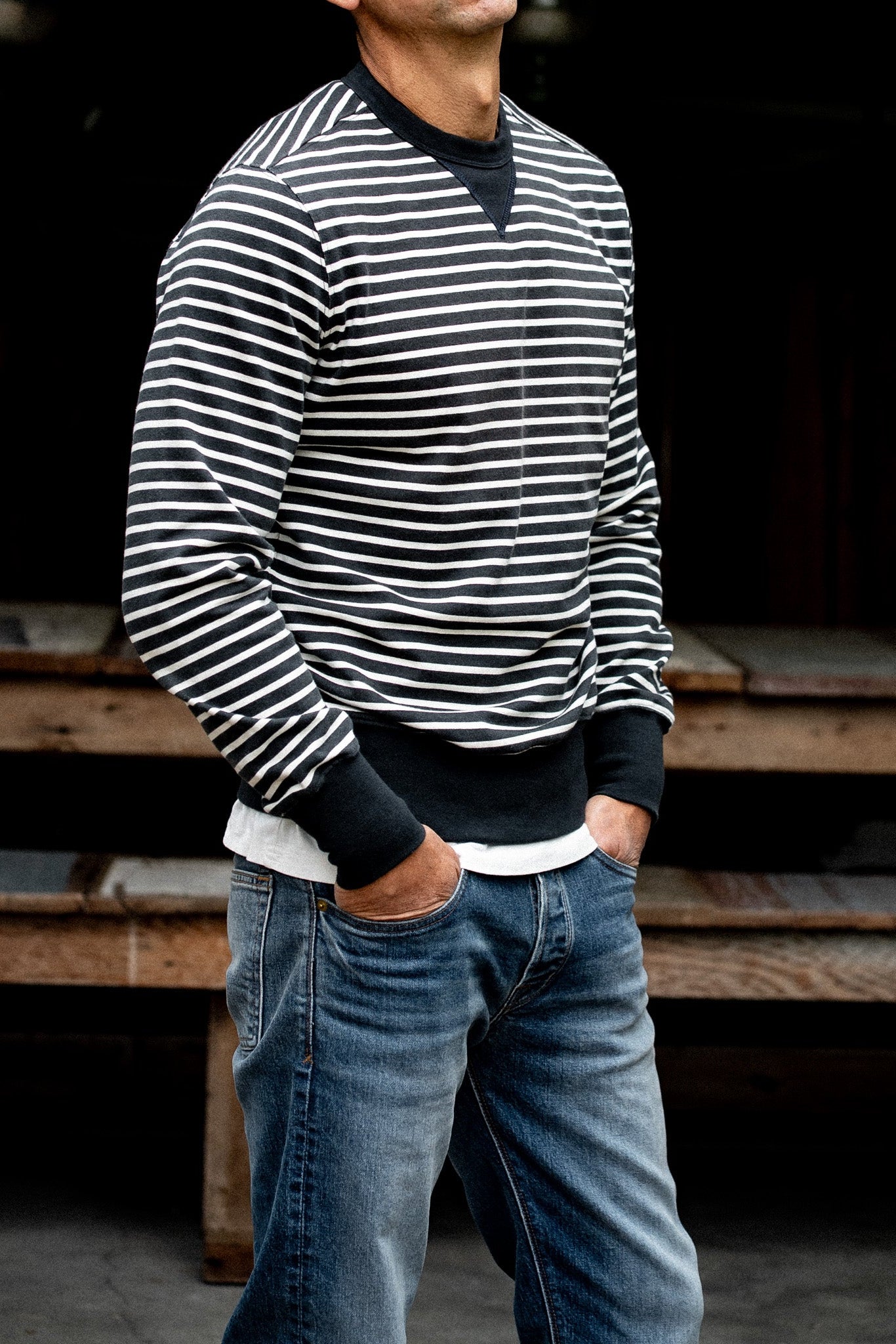 Man wearing a black and white striped rugby jersey pullover with jeans, hands in pockets.