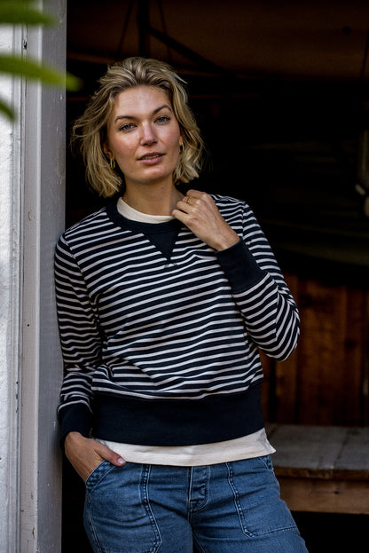 Woman in a black and cream striped Stinson rugby jersey pullover with jeans, leaning in a doorway.