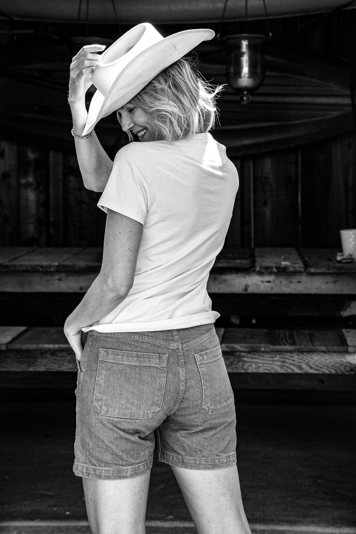 Back view of wheat women's denim shorts with patch pockets, styled with a cowboy hat.