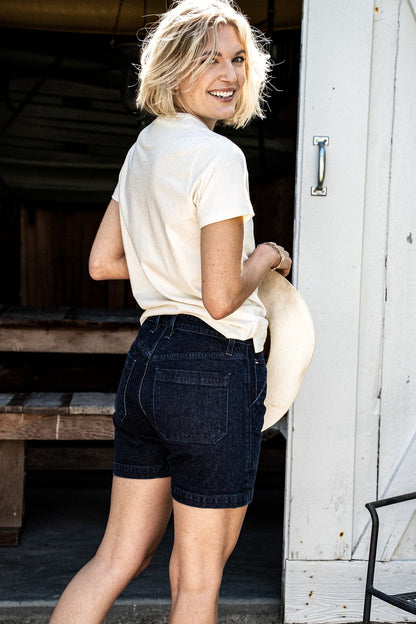 Back view of the Scout military short in ocean wash denim, paired with a cream tee and sun hat.