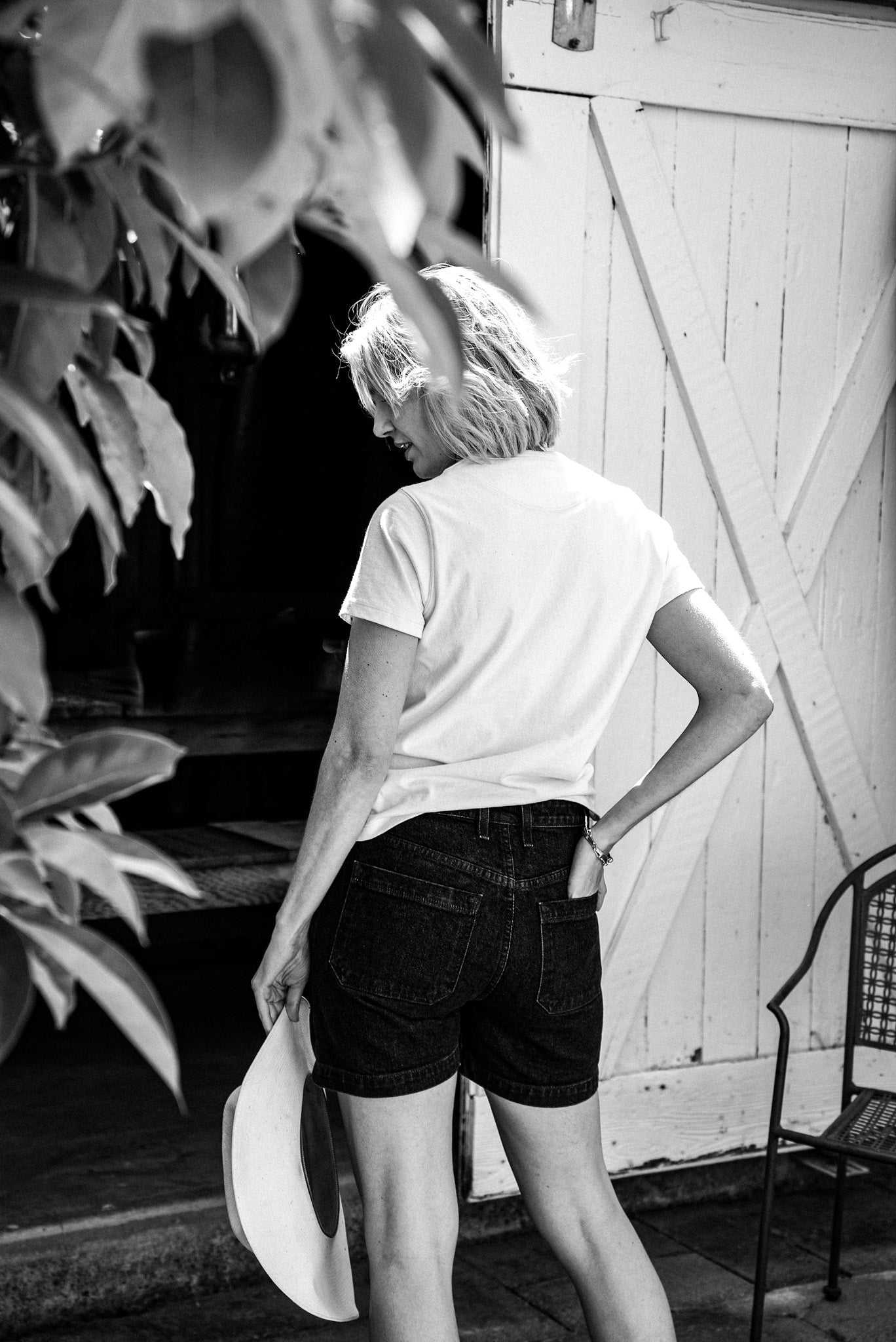 Back view of the Scout denim military shorts in ocean wash, styled with a white tee by a barn door.