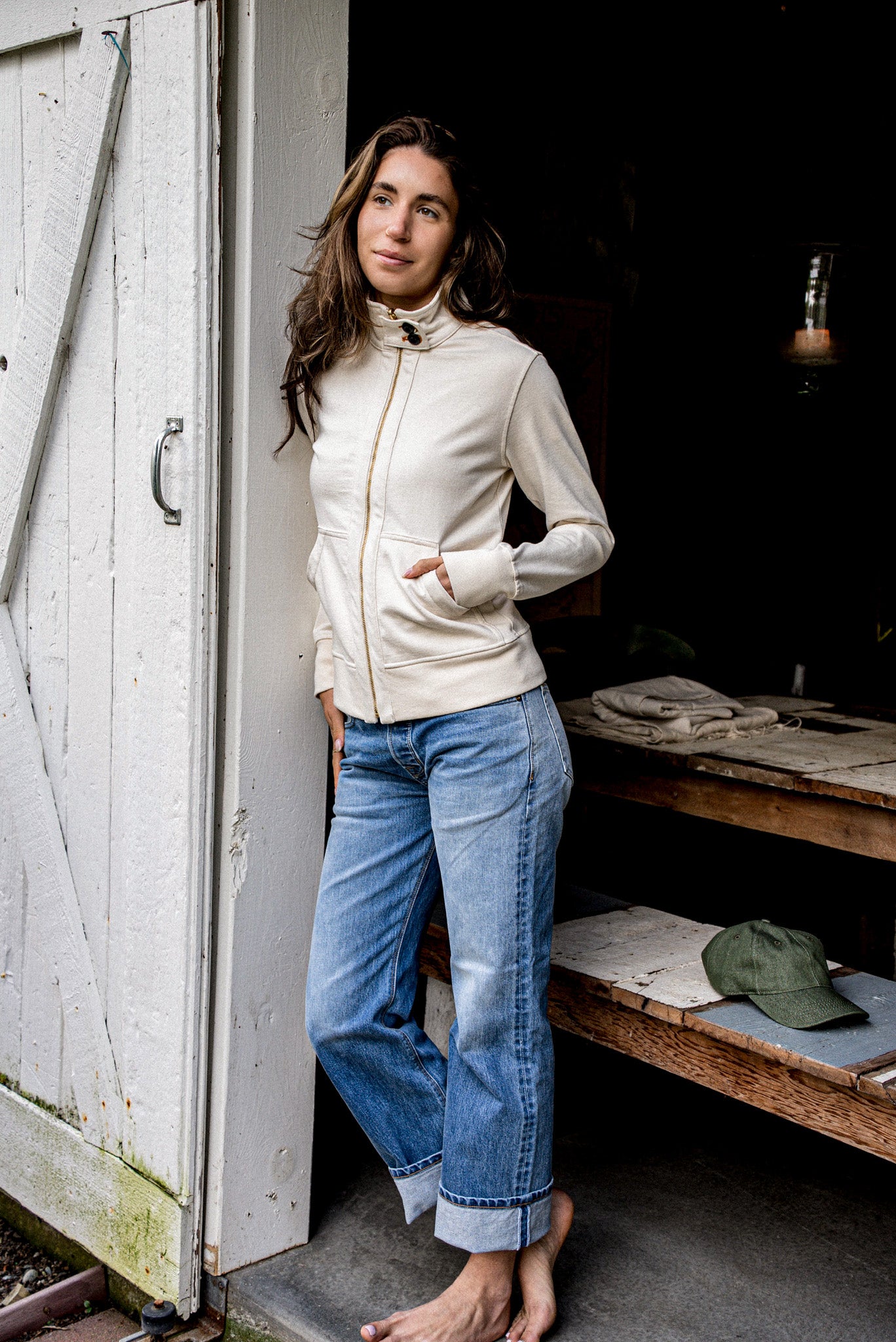 Woman in a natural cotton moto jacket with brass zip, leaning against a weathered barn door.