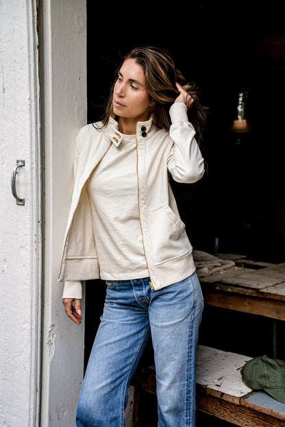 Person wearing a natural cotton Stinson moto jacket with brass zipper over jeans in a doorway.