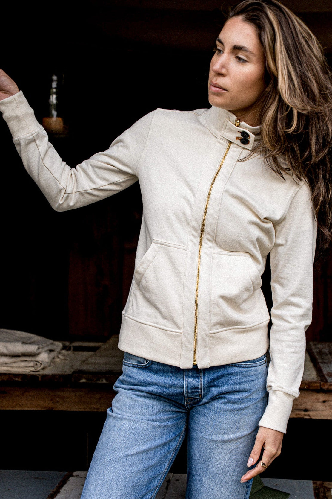 Natural cotton moto jacket with angled brass zipper, worn open over blue jeans.