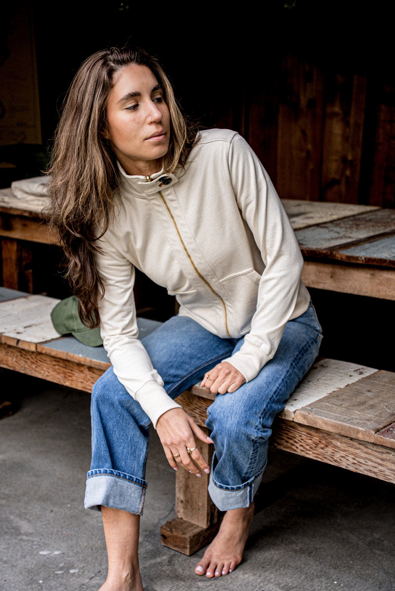 Natural cotton moto jacket with brass zip pull, styled over blue jeans on a bench.