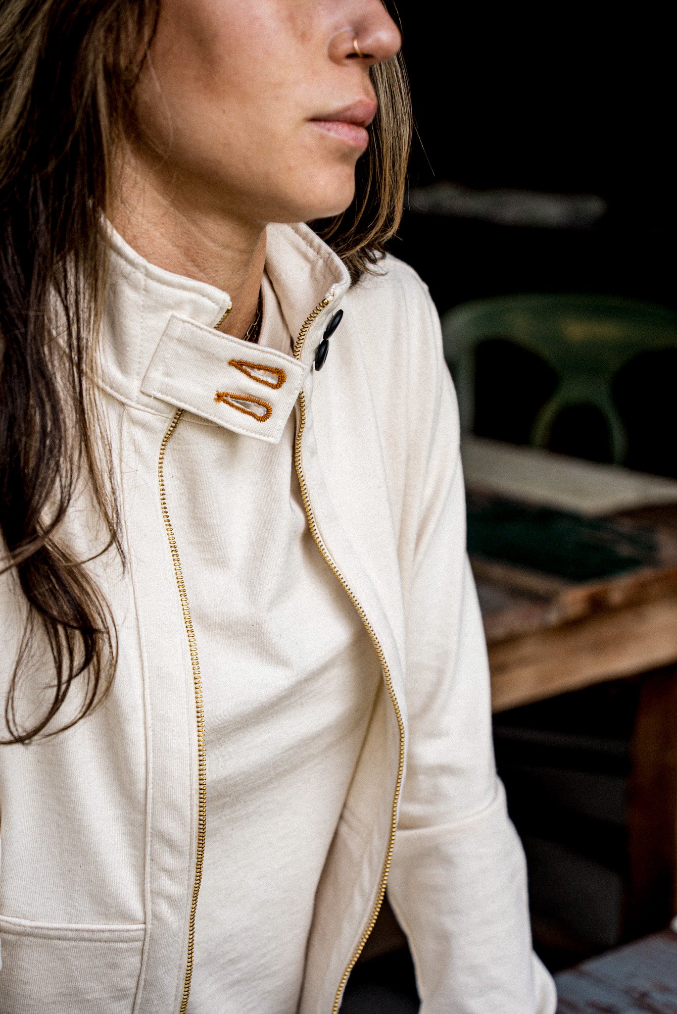 Detail of a natural cotton moto jacket collar with brass zipper and black snap buttons.