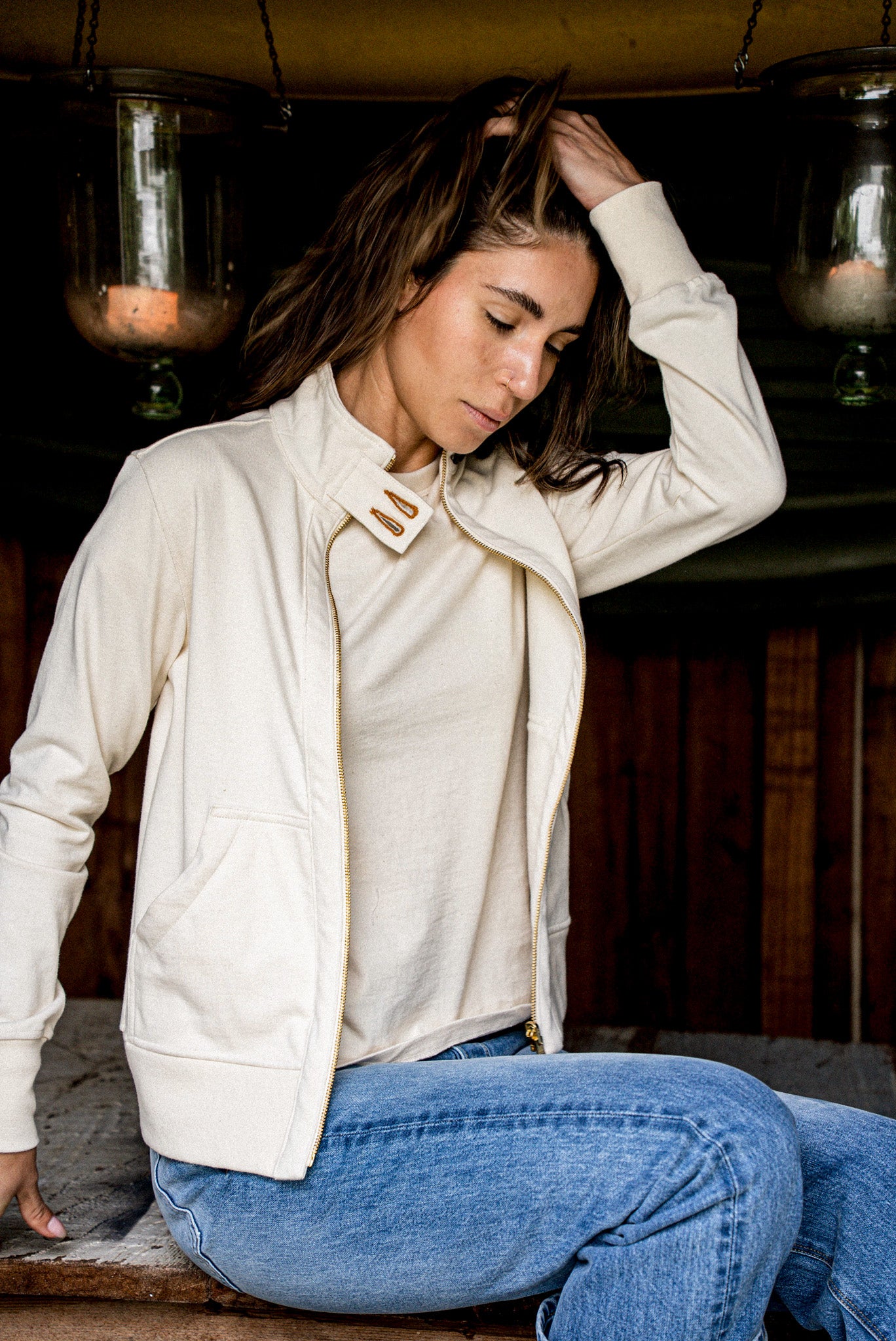 Woman wears an unzipped natural cotton Stinson moto jacket with brass zipper, styled over jeans.