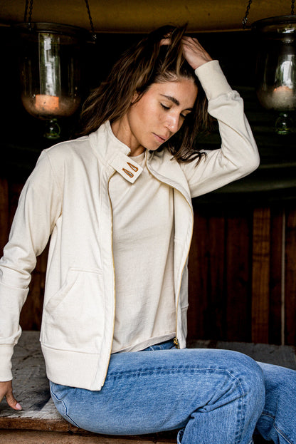 Woman wears an unzipped natural cotton Stinson moto jacket with brass zipper, styled over jeans.