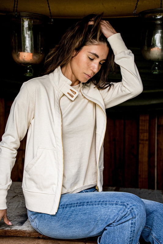 Woman wears an unzipped natural cotton Stinson moto jacket with brass zipper, styled over jeans.