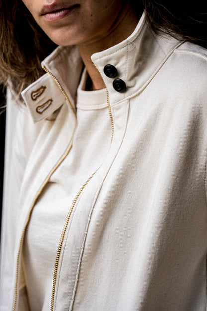Close-up of a natural cotton moto jacket's stand collar, brass zipper, and black buttons.