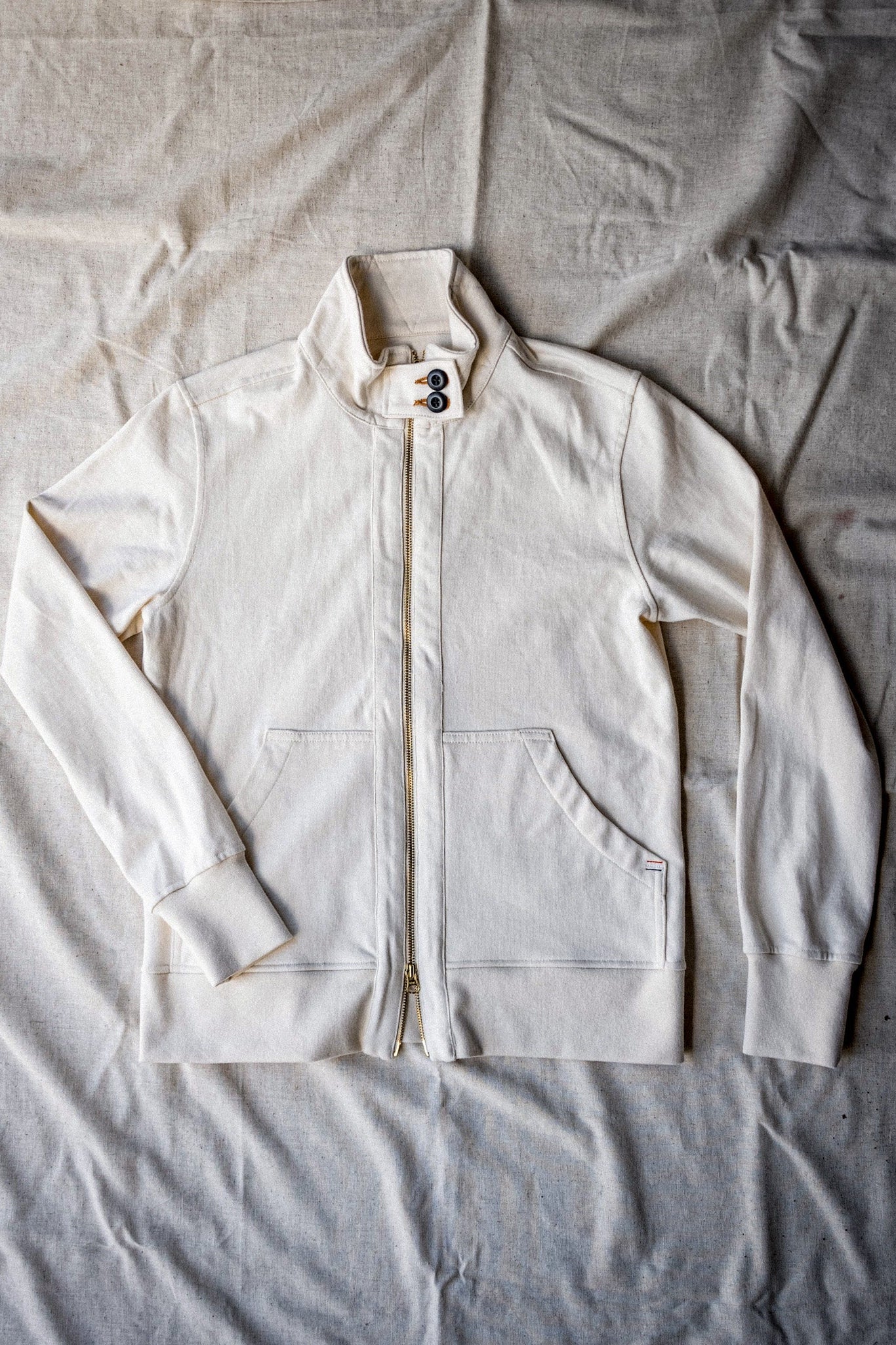 Women's natural cotton moto jacket laid flat with brass zip and stand collar.