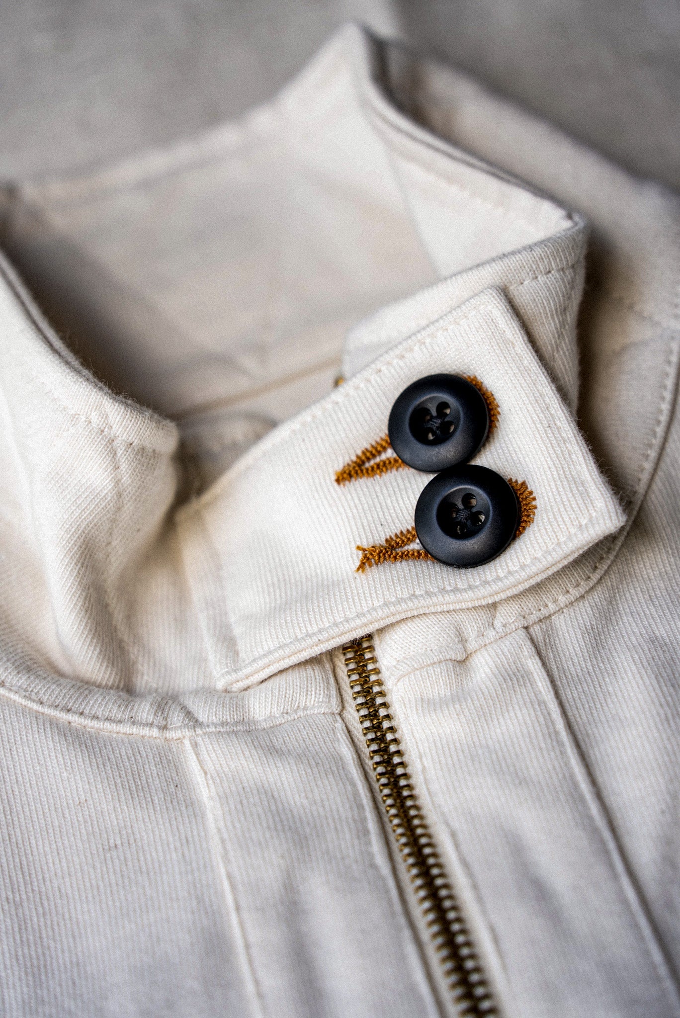 Detail of women's natural cotton moto jacket collar with black buttons and brass zipper.