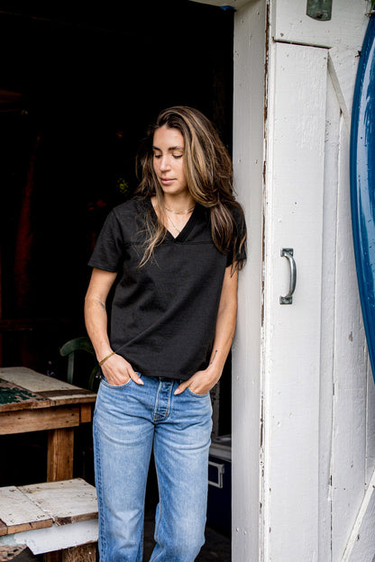 Leaning in a doorway, a person wears the Basalt V-neck cotton jersey with blue jeans.