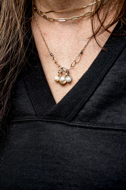 Close-up of a black V-neck cotton jersey top with layered gold pearl necklaces.