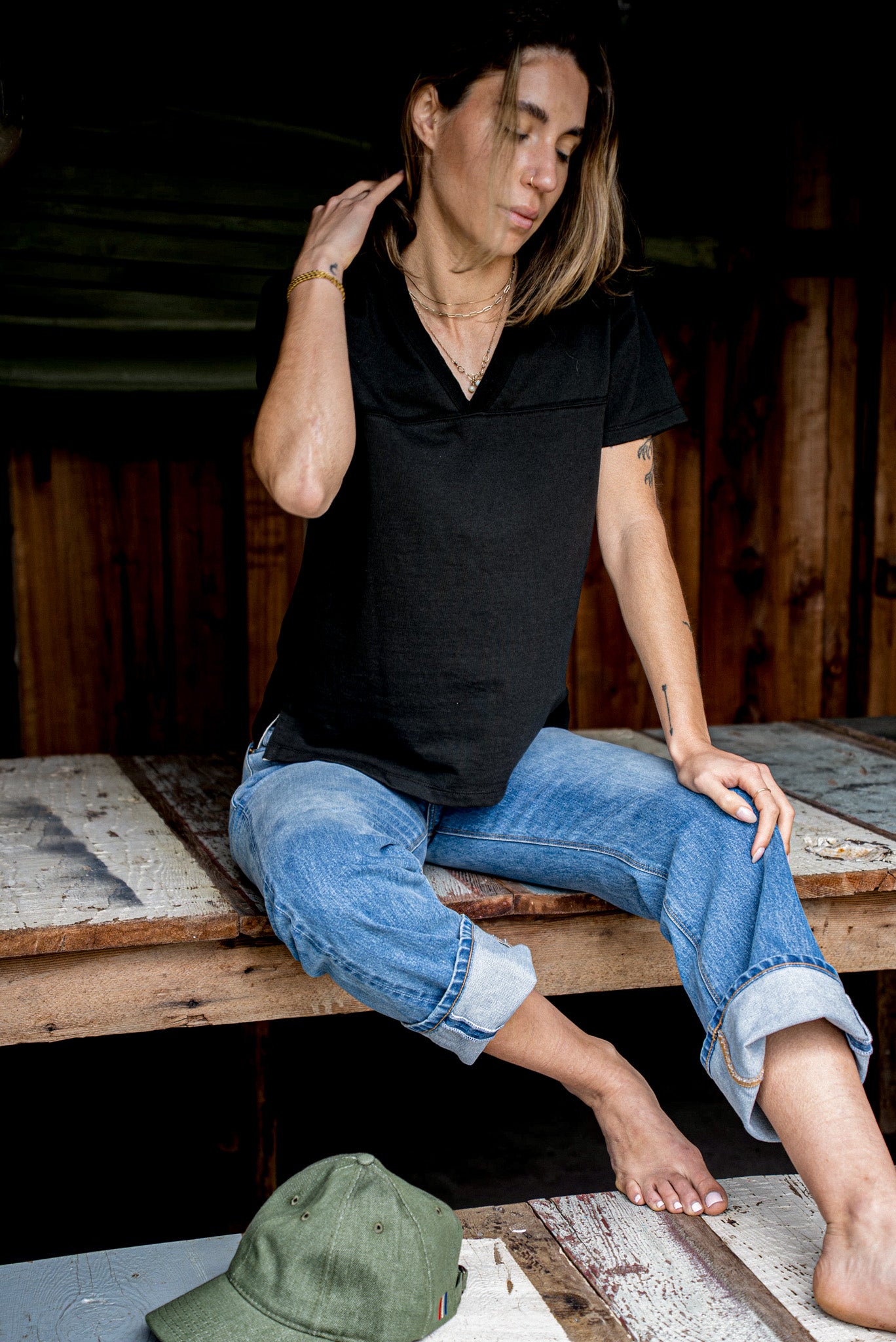 Person in a relaxed black V-neck jersey tee and cuffed blue jeans on weathered planks.