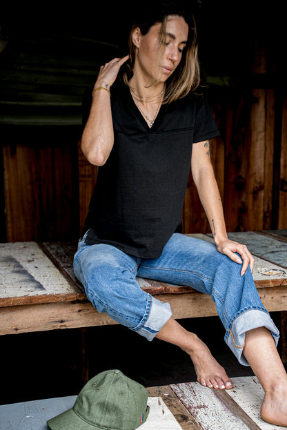 Person in a relaxed black V-neck jersey tee and cuffed blue jeans on weathered planks.