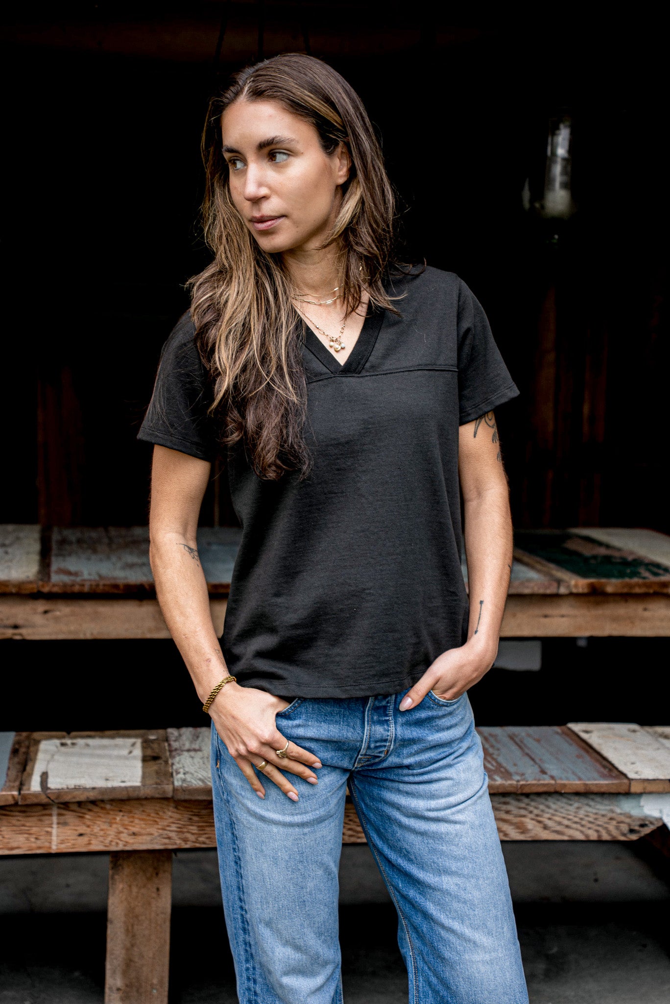 Person wearing basalt black Stinson V-neck cotton jersey tee with jeans by a rustic bench.