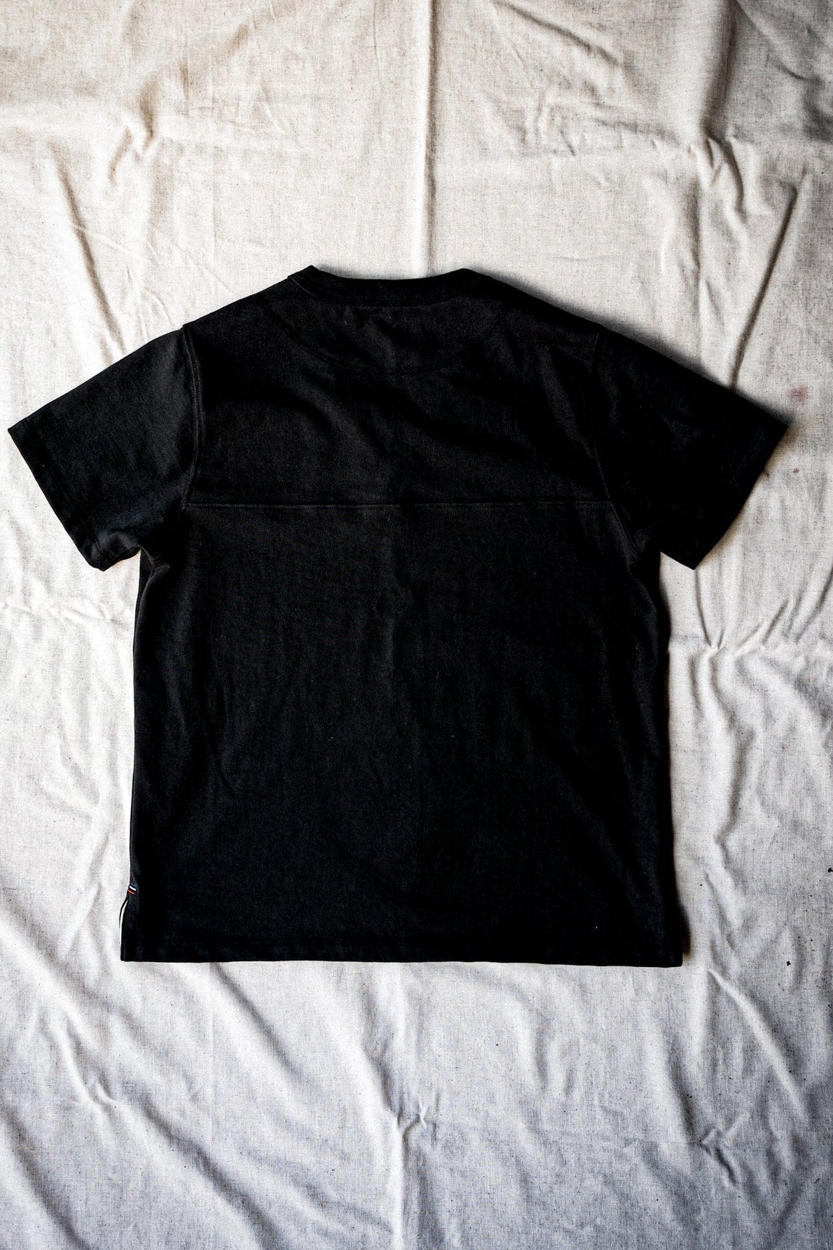 Basalt black cotton jersey tee shown from the back, flat-laid with visible yoke seam.